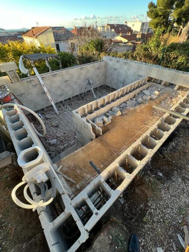 Construction d'une piscine en béton, vue du chantier avec des matériaux et outils visibles.