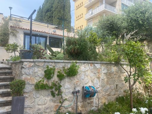 Maison entourée de verdure, avec un jardin bien entretenu et des escaliers en pierre.