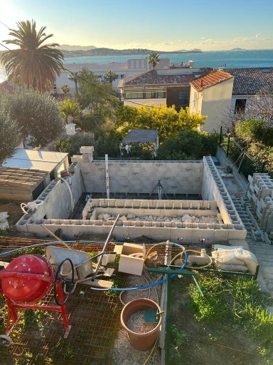 Vue d'une construction inachevée surplombant la mer, avec outils et végétation environnante.