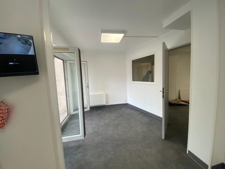 Espace vide avec murs blancs, sol gris, porte noire et matériel de construction.