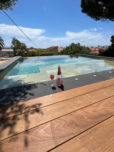 Verre de cocktail à côté d'une piscine, vue sur le ciel et la végétation environnante.