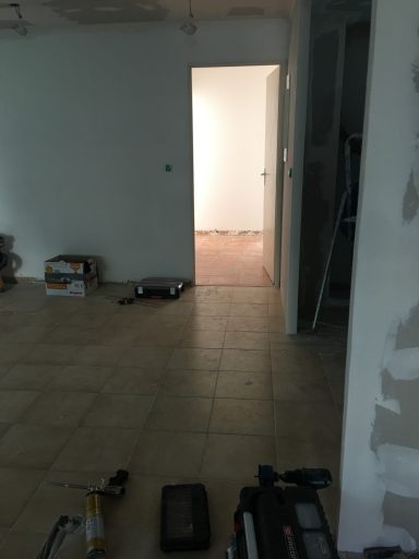 Pièce non meublée avec des outils au sol et une porte menant à une autre pièce.