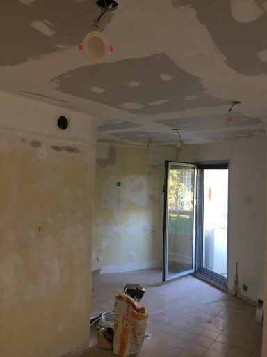 Salle en cours de rénovation, murs dénudés, plafond avec spots, porte-fenêtre ouverte.
