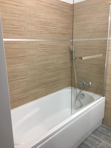 Salle de bain moderne avec baignoire et paroi en verre, carrelage marron et gris.