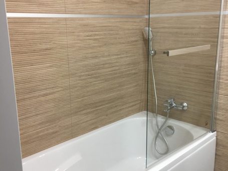 Salle de bain moderne avec baignoire, douche en verre et carrelage en bois clair.